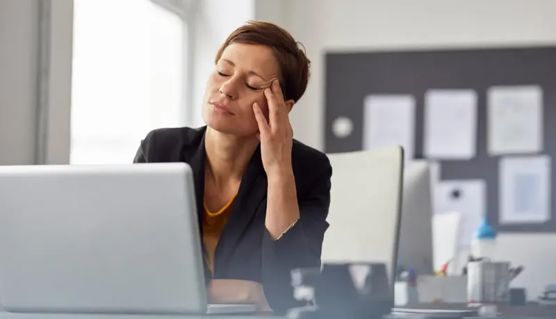 Une femme assise à un bureau, la tête dans les mains, semblant stressée ou préoccupée.