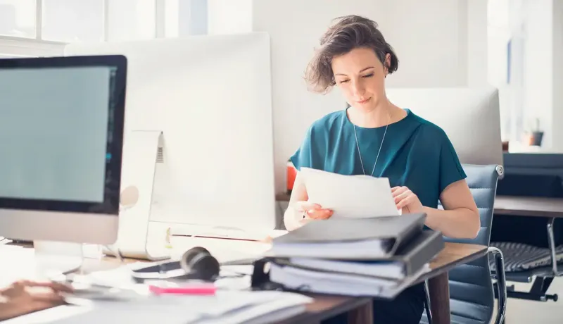 Une femme est assise à un bureau avec un ordinateur consultant des documents