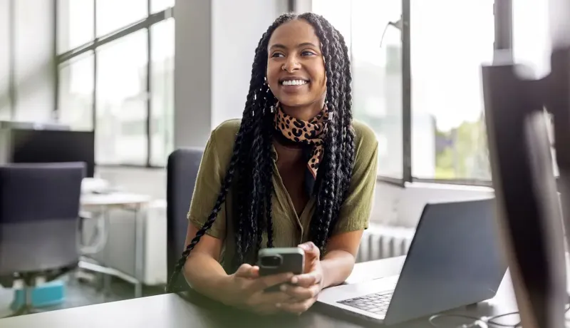 Femme souriante avec des dreadlocks assise à un bureau, utilisant un ordinateur portable.