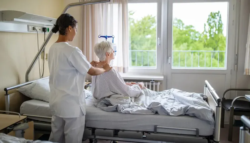 Une aide-soignante aide une femme âgée alitée dans un hôpital, offrant soutien et soins attentifs.