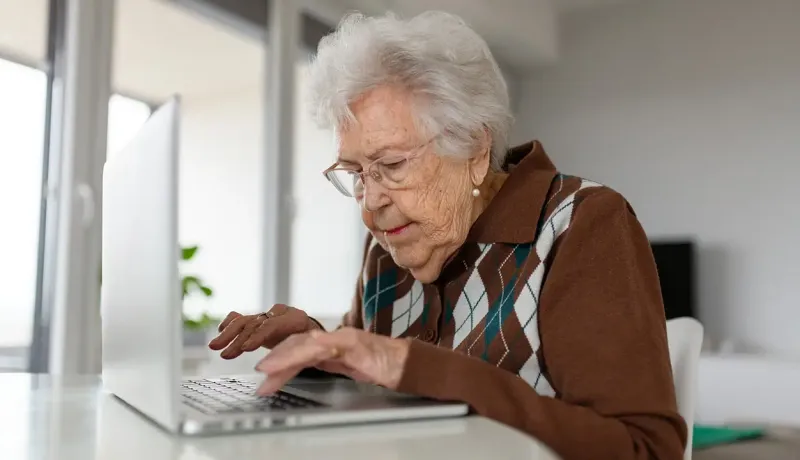 Une femme âgée utilise un ordinateur portable, concentrée sur l'écran.