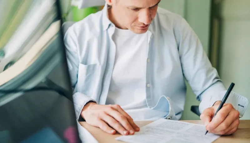 Un homme écrit sur une feuille de papier avec un stylo