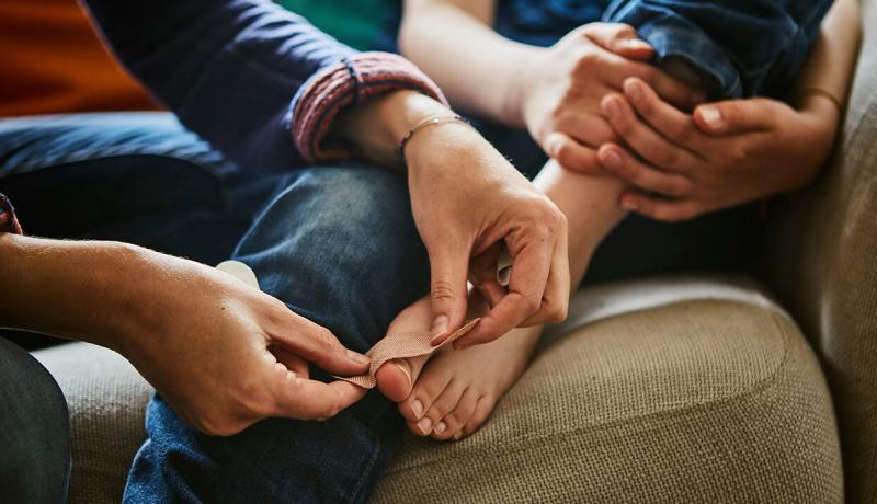 Une femme met un pansement sur le pied de son enfant qui s'est coupé.