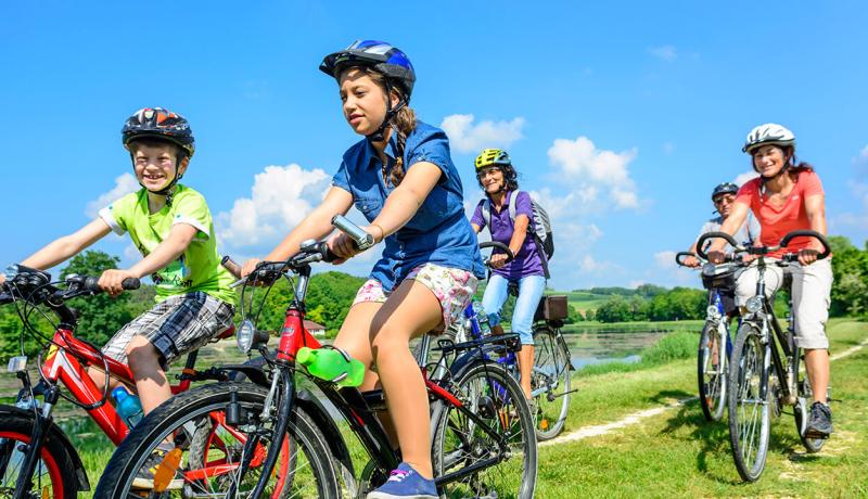 Une famille pédale joyeusement à vélo par une journée ensoleillée, entourée de nature.