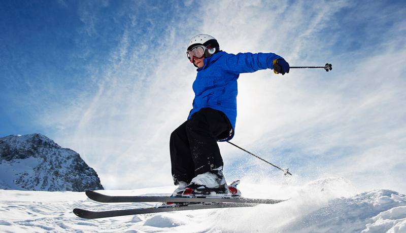 Un enfant en équipement de ski réalise un saut sur une montagne couverte de neige.