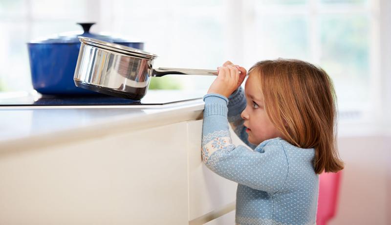 Une enfant saisit une casserole d'eau bouillante sur le comptoir, s'exposant à un danger de brûlure.