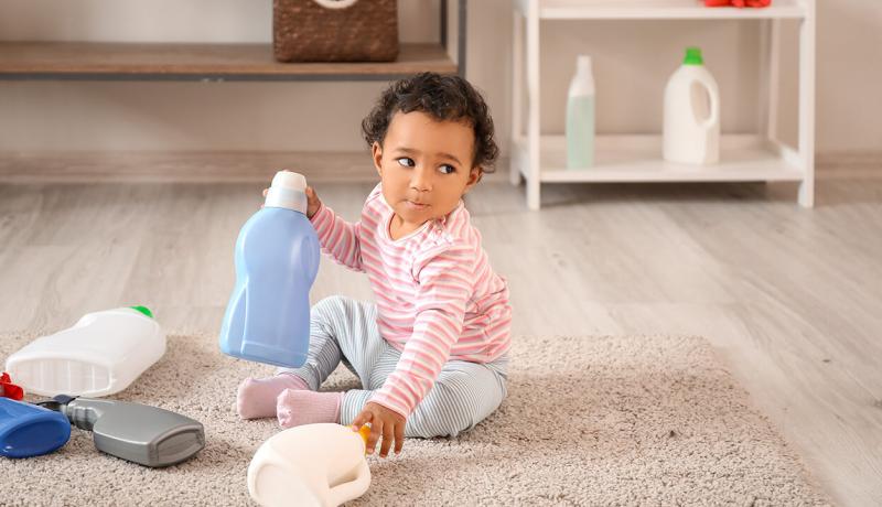 Une petite enfant joue avec des produits de nettoyage sur le sol.