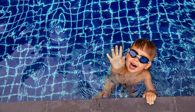 Un enfant portant des lunettes de natation cherche de l'aide pour sortir de la piscine.
