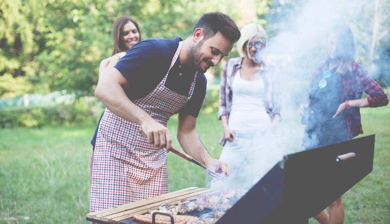 Dans un jardin, un homme grille de la viande au barbecue, tandis que des amis profitent de l'ambiance conviviale.