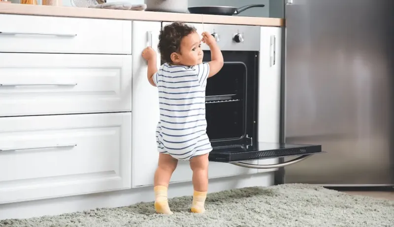 Un jeune enfant debout touche à la porte ouverte d'un four.