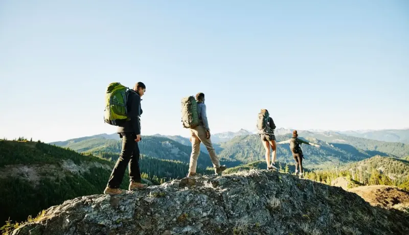 Groupe de randonneurs équipés de sacs à dos marchant sur une crête rocheuse face à un panorama montagneux.