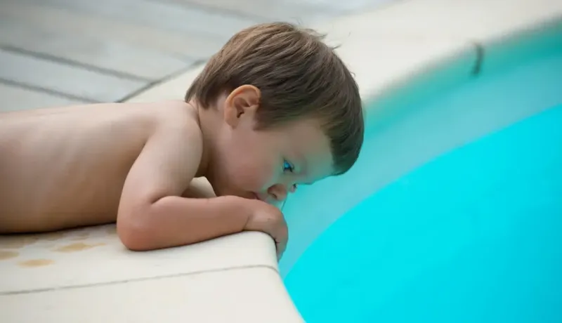 Un petit enfant penché très près du rebord d'une piscine, illustrant les risques de chute et de noyade.