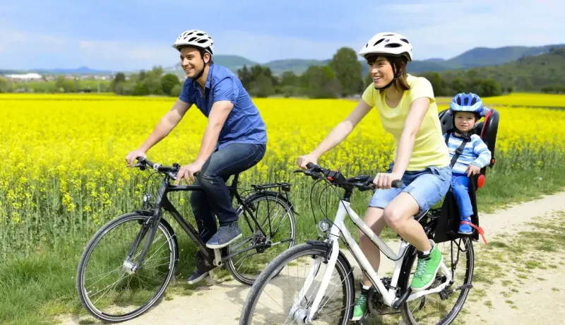 Un couple et un enfant dans un siège sécurisé font une balade à vélo le long d'un champ de fleurs.