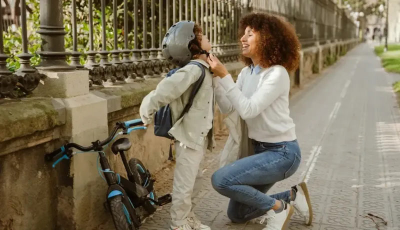 Une femme attache avec soin le casque de protection d'un jeune garçon avant une sortie à vélo en ville.