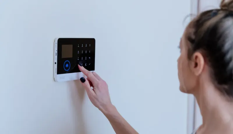 Une femme utilise son index pour entrer un code sur le tableau de bord numérique d'un système de sécurité résidentiel.