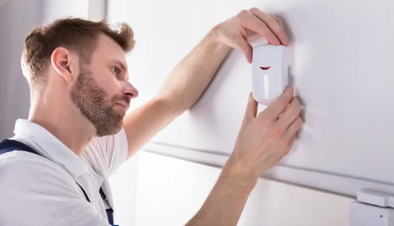 Spécialiste de la sécurité fixant un dispositif de détection de présence (PIR) à un mur d'une pièce.