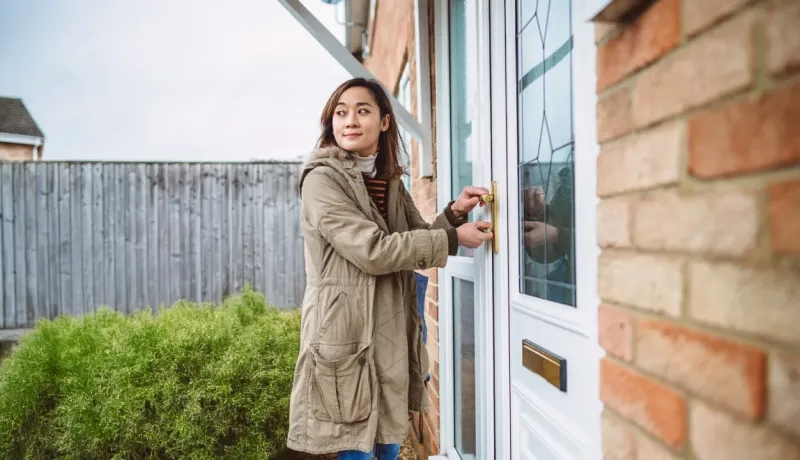 Une femme ouvre la porte d'une maison tout en regardant derrière elle. 