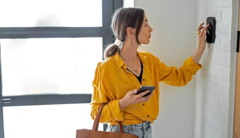 Femme moderne utilisant une borne de contrôle de porte ou de sécurité à l'entrée d'une maison lumineuse.