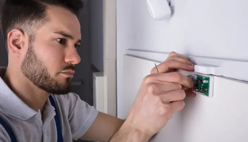 Électricien fixant et connectant la petite carte électronique d'un capteur de sécurité domestique.