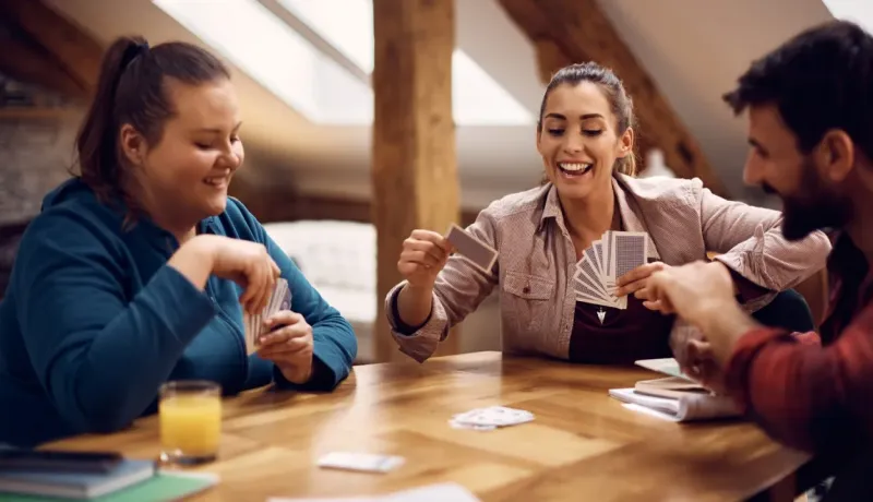 Trois colocataires joyeux partagent un moment amusant autour d'une table en bois en jouant à un jeu de cartes.