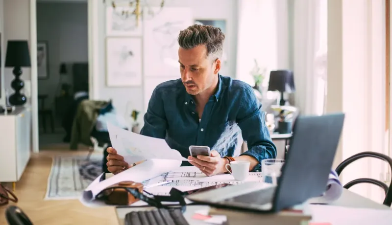Homme concentré travaillant sur des plans et documents, utilisant son téléphone portable.