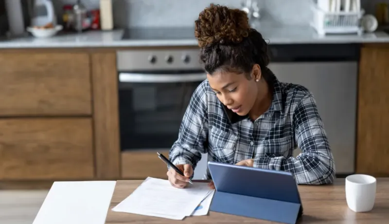 Femme en chemise à carreaux écrivant sur des papiers et téléphonant.