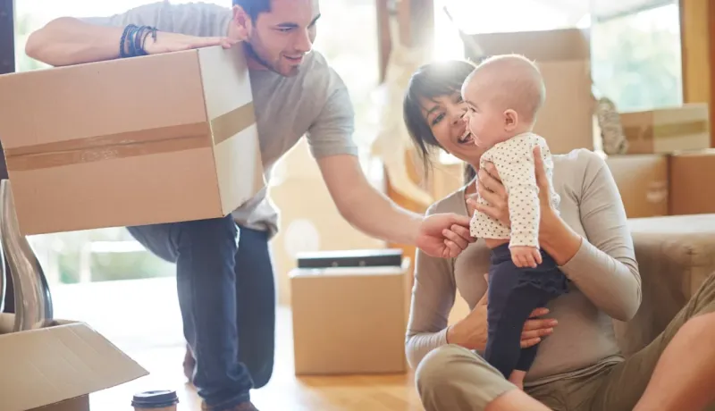 Couple avec bébé au milieu de cartons, emménageant dans leur nouvelle maison. L'homme tient une boîte en carton.