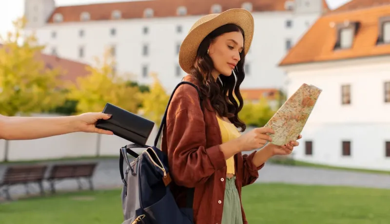 Femme touriste regardant une carte. Une main vole son portefeuille dans son sac à dos (vol à la tire).