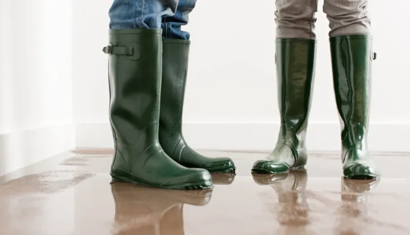 Deux personnes portant des bottes en caoutchouc vert se tiennent dans une pièce inondée. 