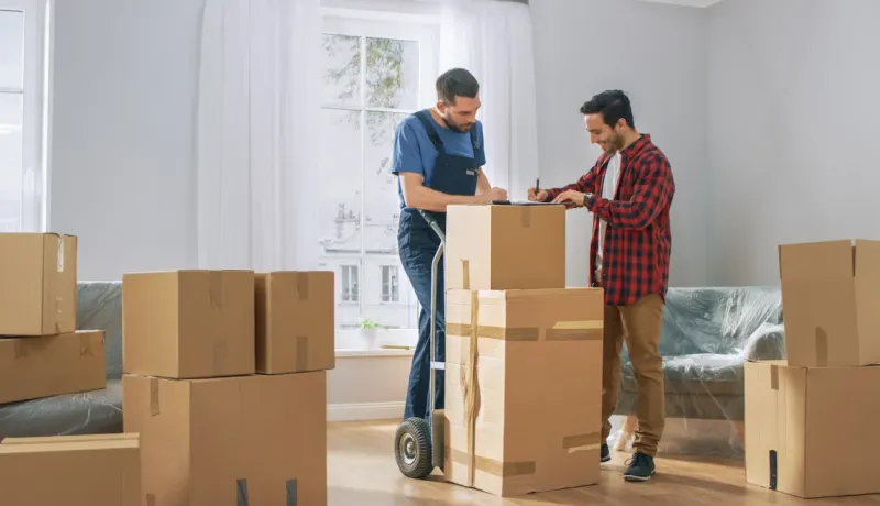Déménageur et client devant une pile de cartons signant un document de livraison dans une pièce vide.