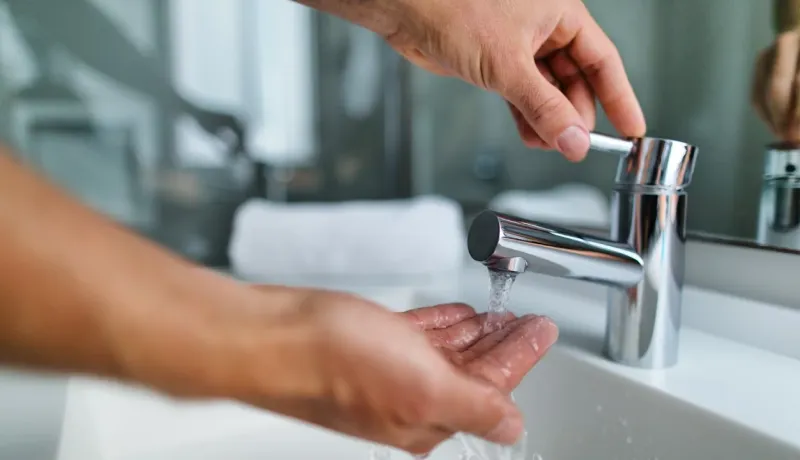 Gros plan sur une main ajustant le robinet d'un lavabo moderne, l'eau coule sur l'autre main.