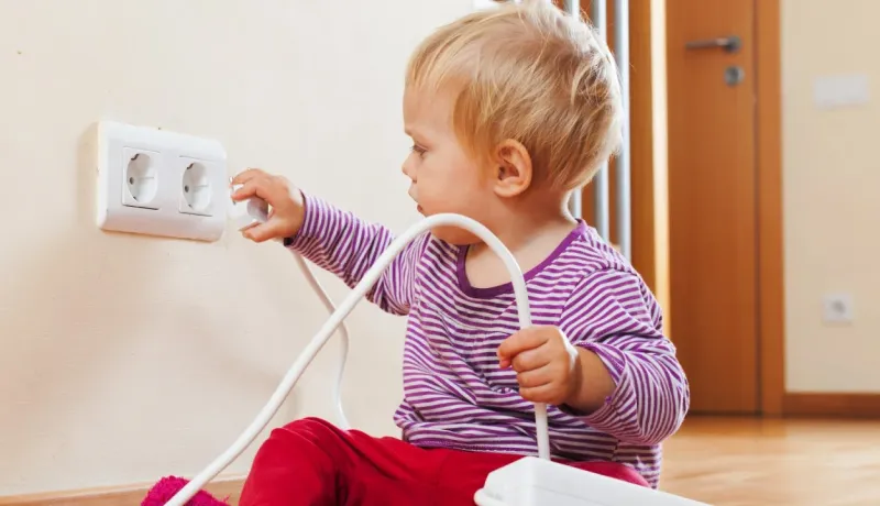 Un tout-petit joue près d'une prise électrique, montrant un comportement potentiellement dangereux.