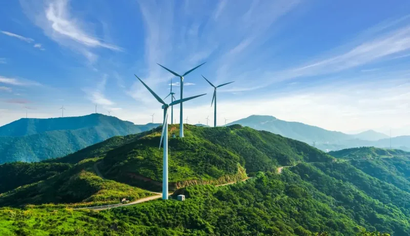 Plusieurs éoliennes installées sur des collines verdoyantes sous un ciel bleu clair, illustrant l'énergie propre.