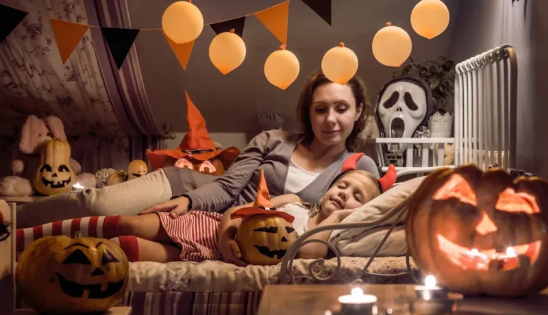 Une mère et sa fille déguisée se détendent dans une chambre décorée pour Halloween avec des citrouilles sculptées.