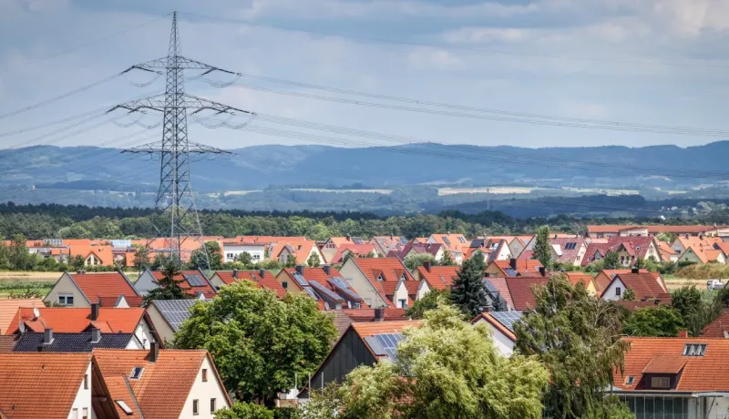 Vue aérienne d'un quartier de maisons aux toits rouges, dominé par un grand pylône électrique et ses lignes.