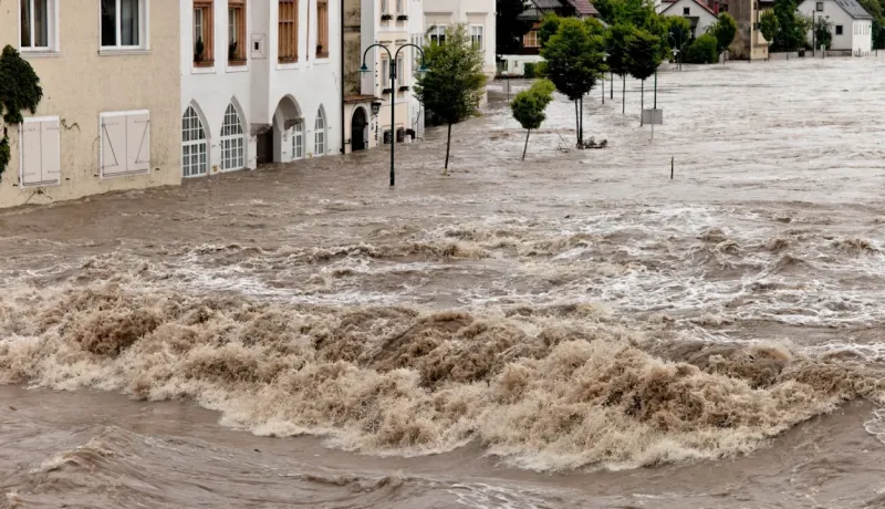 Fortes inondations: l'eau marron et agitée déferle dans une rue, atteignant les façades d'immeubles anciens.