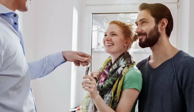 Agent immobilier remettant les clés à un couple souriant et ravi, marquant l'achat de leur nouvelle maison.