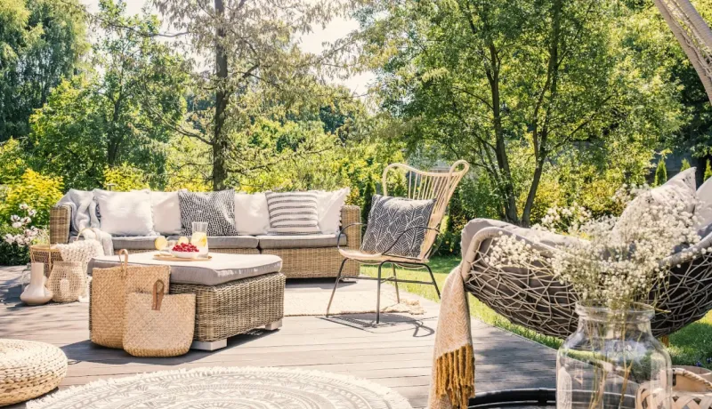 Jolie terrasse en bois aménagée dans un jardin luxuriant, avec un canapé d'extérieur, une balançoire et des paniers en osier.