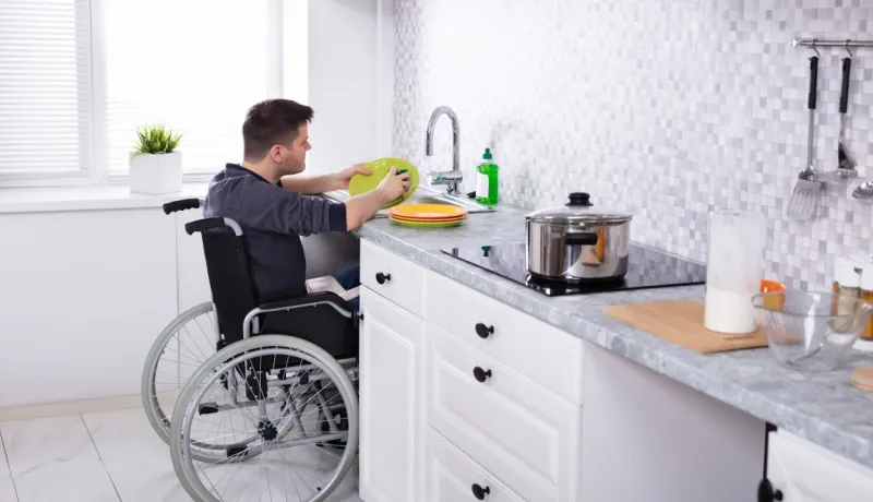Homme en fauteuil roulant lavant la vaisselle dans une cuisine adaptée ou accessible.