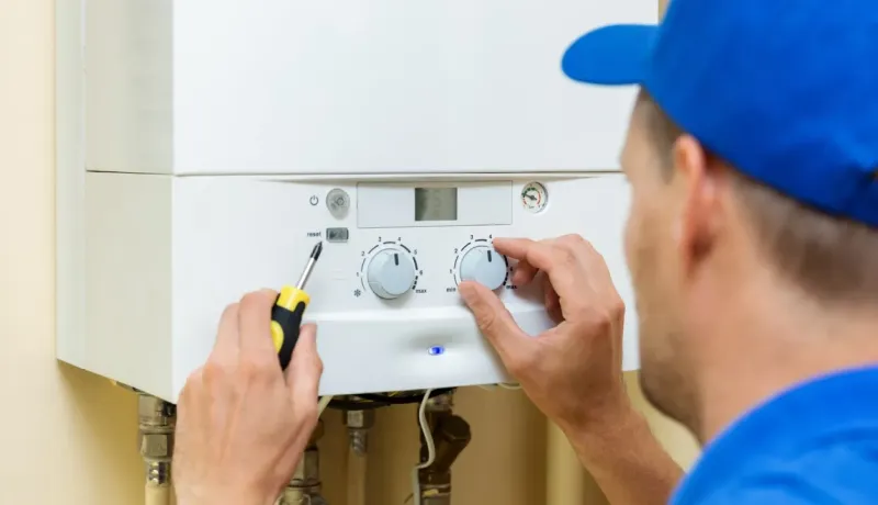Gros plan sur un technicien en casquette bleue ajustant les commandes d'une chaudière murale blanche.