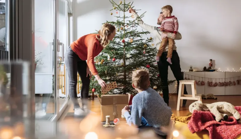 Famille décorant un grand sapin de Noël ensemble dans leur salon lumineux, les enfants aidant les parents.