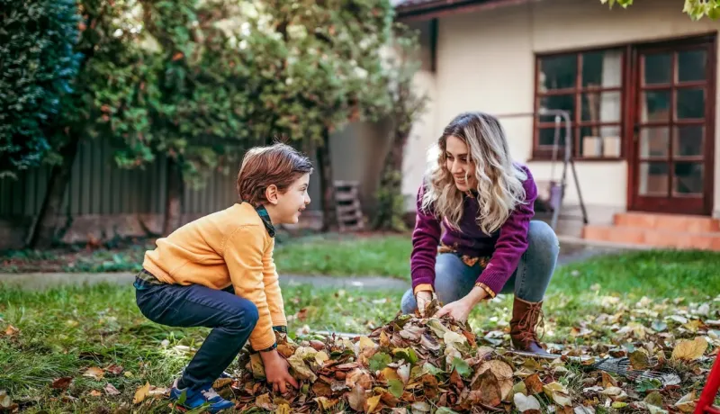 Mère et fils s'amusant à ramasser un tas de feuilles mortes dans le jardin, en automne.