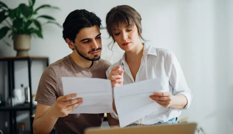 Jeune couple s'appuyant l'un contre l'autre, lisant attentivement des documents à la maison.