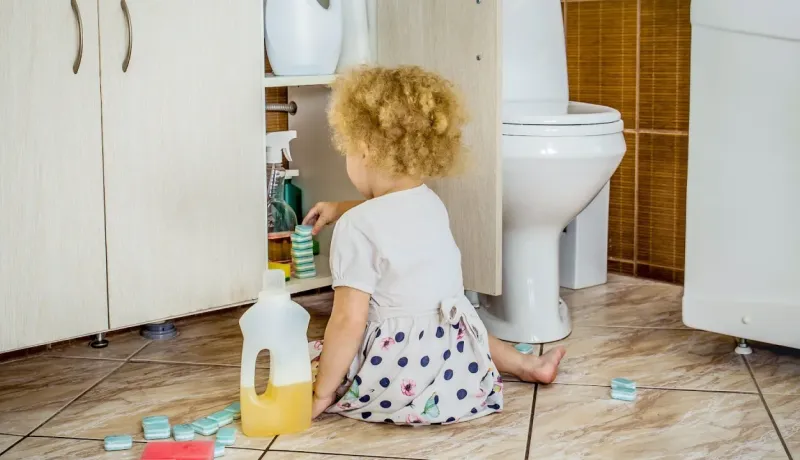 Jeune enfant jouant avec des produits de nettoyage stockés sous un meuble de salle de bain, près des toilettes.