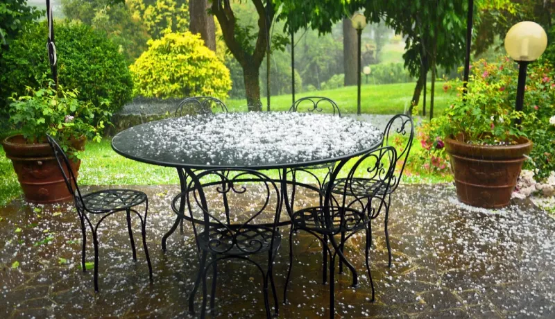 Meubles de jardin en fer forgé recouverts de grêle, sous une forte pluie dans un jardin.