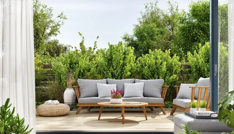 Vue depuis l'intérieur sur une élégante terrasse en bois avec salon de jardin, entourée de verdure luxuriante.
