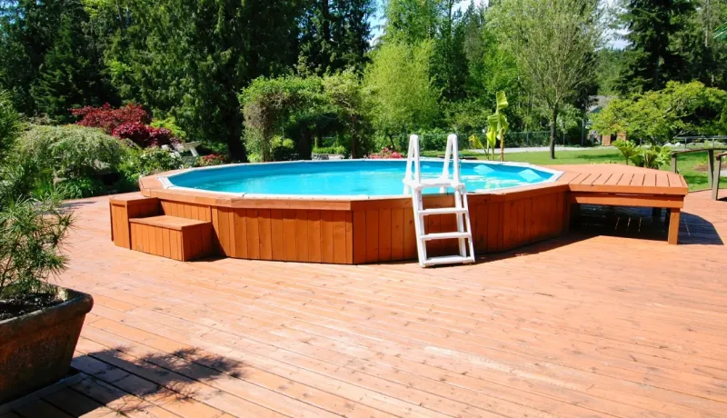 Une piscine hors sol octogonale en bois, entourée d'une terrasse en bois, dans un jardin verdoyant.