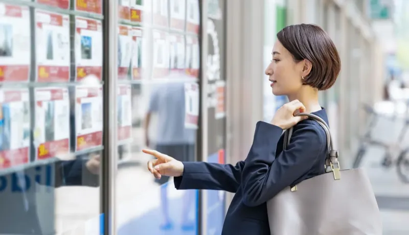 Une femme en tenue de travail regarde les annonces immobilières affichées dans la vitrine d'une agence.