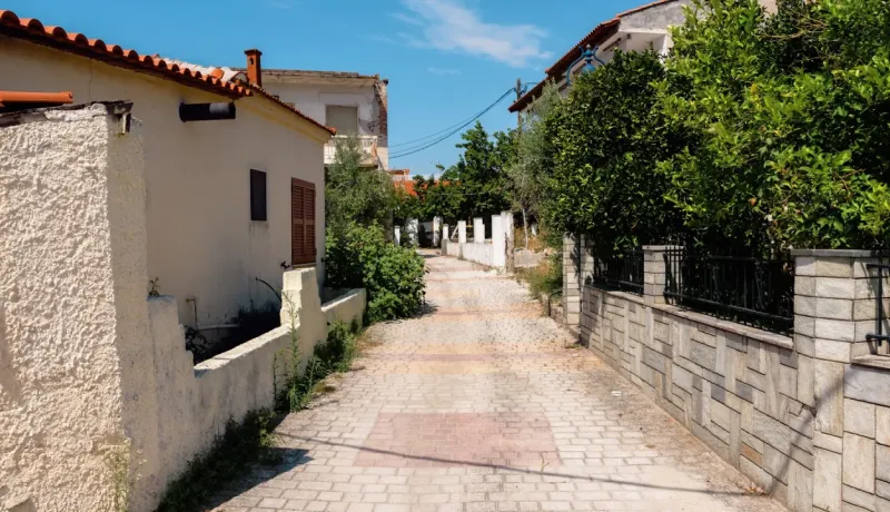Une ruelle pavée étroite bordée de vieilles maisons en plâtre blanc et d'une végétation luxuriante dans un village ensoleillé.
