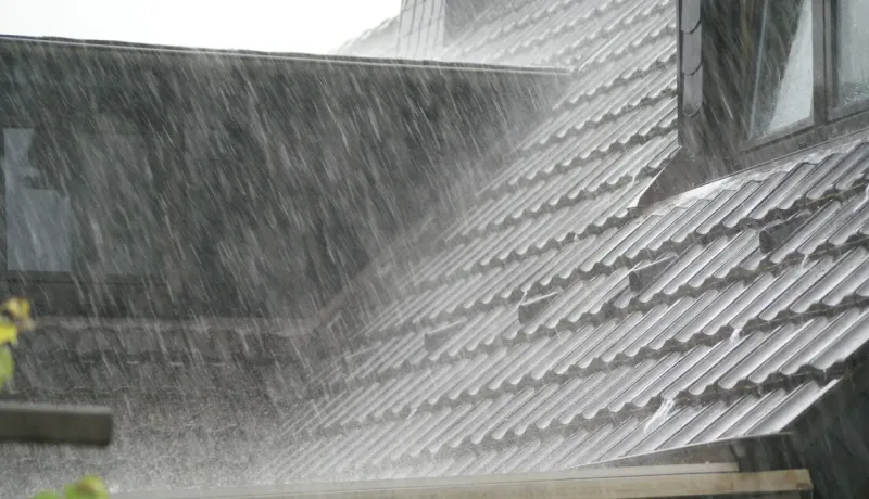Gros plan sur un toit en tuiles sombres, sous une forte pluie, l'eau s'écoulant par la gouttière.
